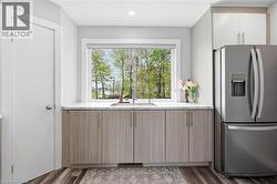 Kitchen featuring a double basin stainless steel sink, a stainless steel French door refrigerator, light-toned wood-finish cabinetry, white upper cabinetry, and a light-colored countertop - 