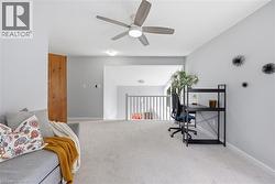 Carpeted loft area featuring a ceiling fan with integrated lighting, natural wood-finish door, and a white railing overlooking a lower level - 