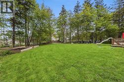 Expansive green lawn surrounded by mature trees, featuring multiple raised garden beds, a wooden deck, and additional exterior seating - 