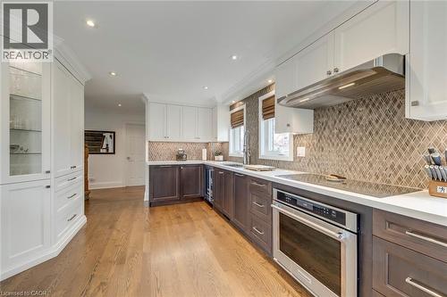 Two tone kitchen with two tone color scheme, oven, light wood-style floors, glass insert cabinets, and crown molding - 3311 Springvale Court, Burlington, ON - Indoor Photo Showing Kitchen With Upgraded Kitchen