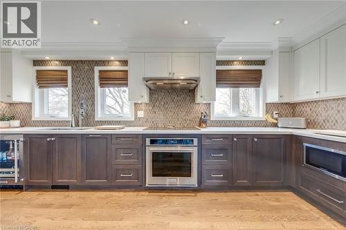 Kitchen featuring two tone cabinets, oven, wine cooler, ornamental molding, and backsplash - 3311 Springvale Court, Burlington, ON - Indoor Photo Showing Kitchen With Upgraded Kitchen