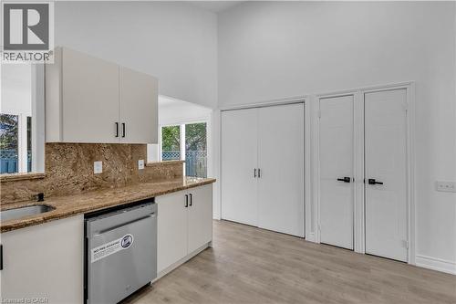 Kitchen area featuring light-toned cabinetry with dark hardware, a stainless steel dishwasher, and stone countertops extending to a matching backsplash - 375 Silverbirch Boulevard, Hamilton, ON - Indoor Photo Showing Kitchen