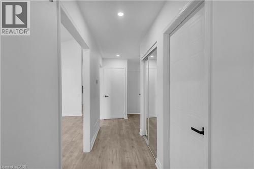 Hallway featuring light wood-finish flooring, white walls, recessed ceiling lighting, a mirrored closet door, and white paneled doors with black hardware - 375 Silverbirch Boulevard, Hamilton, ON - Indoor Photo Showing Other Room