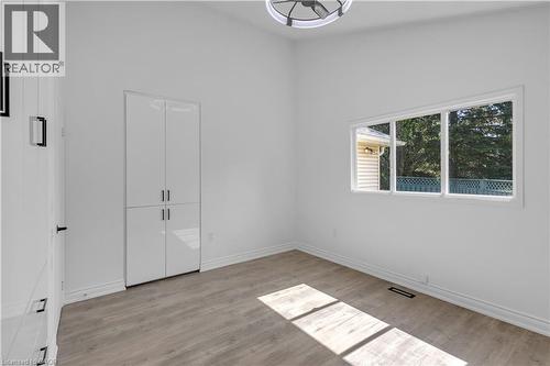 Spacious room featuring light wood-finish flooring, a large multi-pane window, built-in white high-gloss cabinetry, and a contemporary ceiling fixture - 375 Silverbirch Boulevard, Hamilton, ON - Indoor Photo Showing Other Room