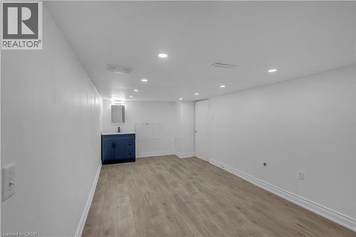 Spacious room featuring light wood-finish flooring, recessed ceiling lighting, a dark blue vanity with a white countertop, and a wall-mounted mirror with an attached vanity light - 375 Silverbirch Boulevard, Hamilton, ON - Indoor Photo Showing Other Room