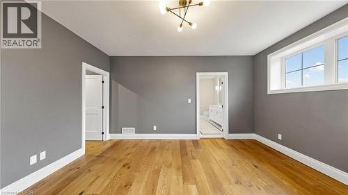 Spacious room featuring wood-finish flooring, neutral gray walls, white trim, a modern ceiling light fixture, and multiple windows - 41 Talbot Road, Delhi, ON - Indoor Photo Showing Other Room