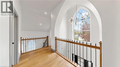 Upper-level landing featuring a grand arched window, wood-finish flooring, a modern chandelier, and iron balusters with wooden handrails - 41 Talbot Road, Delhi, ON - Indoor Photo Showing Other Room