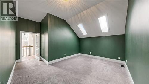 Attic room featuring two skylights, wall-to-wall carpeting, white baseboards, and a doorway with French doors opening to an interior balcony with a black metal railing - 41 Talbot Road, Delhi, ON - Indoor Photo Showing Other Room
