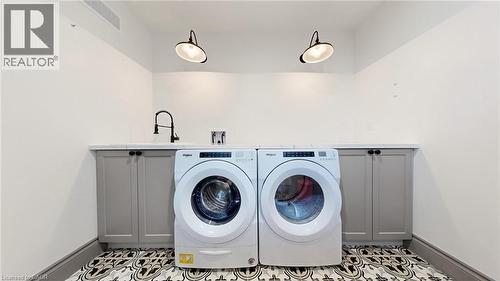 Laundry area featuring patterned floor tile, under-counter cabinetry, a mounted utility sink with a matte black faucet, and two industrial-style wall sconces - 41 Talbot Road, Delhi, ON - Indoor Photo Showing Laundry Room