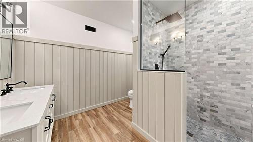 Bathroom featuring wood-finish flooring, board and batten wall paneling, a double vanity with matte black fixtures, a walk-in shower with glass enclosure, and subway tile walls - 41 Talbot Road, Delhi, ON - 