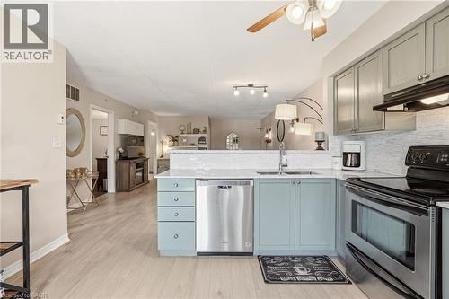 Kitchen featuring light blue cabinetry, stainless steel appliances, a white tile backsplash, and light wood-finish flooring - 1411 Walker'S Line Unit# 105, Burlington, ON - Indoor Photo Showing Kitchen
