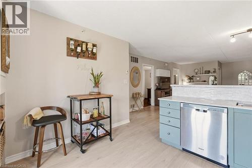Kitchen featuring light blue lower cabinetry, a stainless steel dishwasher, white subway tile backsplash, and light wood-finish flooring - 1411 Walker'S Line Unit# 105, Burlington, ON - Indoor