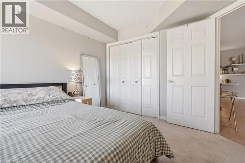 Wall-to-wall carpeting in a neutral tone, featuring a multi-panel closet door system with circular knobs, a paneled interior door with a brass-toned knob, and a doorway opening to a room with wood-fin - 1411 Walker'S Line Unit# 105, Burlington, ON - Indoor Photo Showing Bedroom
