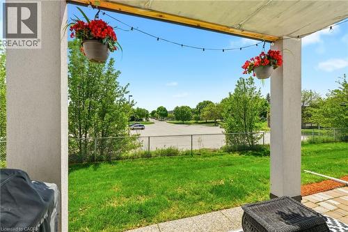 Covered patio featuring string lights, hanging planters with red flowers, a concrete support column, and an adjacent green space - 1411 Walker'S Line Unit# 105, Burlington, ON - Outdoor