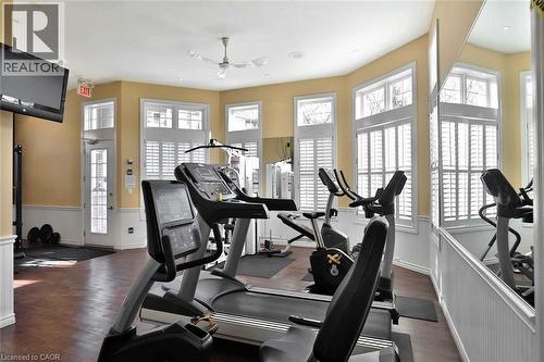 Fitness area featuring wood-finish flooring, multiple windows with plantation shutters, wainscoting, and a ceiling fan - 1411 Walker'S Line Unit# 105, Burlington, ON - Indoor Photo Showing Gym Room