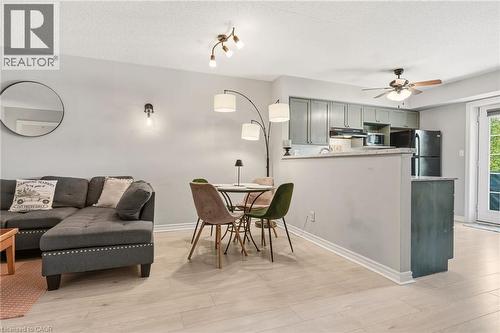 Open-concept living space featuring wood-finish flooring, a kitchen with dark cabinetry, integrated appliances, and a ceiling fan, alongside a dining area and a balcony access door - 1411 Walker'S Line Unit# 105, Burlington, ON - Indoor