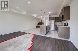 Kitchen featuring a central island with a light-colored countertop, dark wood-finish cabinetry, stainless steel appliances, and light-colored tile flooring - 