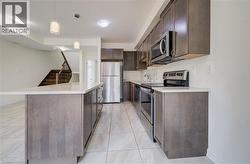 Kitchen featuring a center island with a light-toned countertop, stainless steel appliances, dark wood-finish cabinetry, tile flooring, and integrated lighting - 