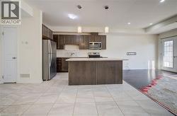 Open-concept kitchen and living area featuring a central island, stainless steel appliances, dark wood-finish cabinetry, and a textured tile backsplash - 