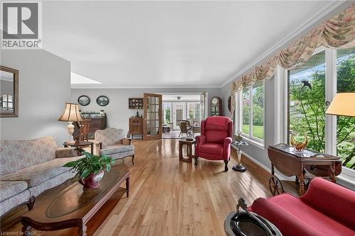 Spacious living area featuring polished wood-finish flooring, a wall of large windows, crisp white crown molding, light gray wall paint, and French doors opening to the sunroom - 2 Summit Circle, Simcoe, ON - Indoor Photo Showing Living Room