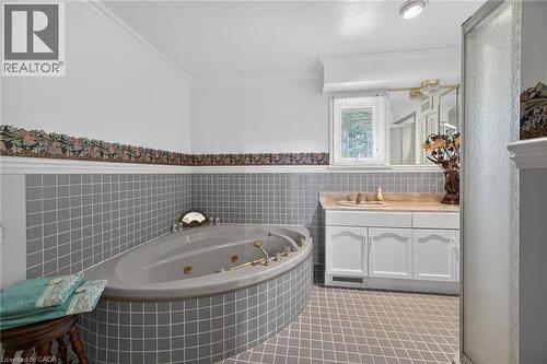 Bathroom featuring an integrated jetted tub with tile surround, a single vanity with a solid surface countertop, white cabinetry, and diamond-patterned tile flooring - 2 Summit Circle, Simcoe, ON - Indoor Photo Showing Bathroom