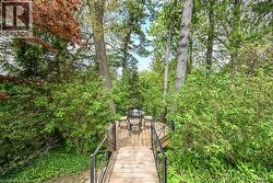 Wood-finish walkway featuring black metal railings and surrounding mature trees and dense foliage - 