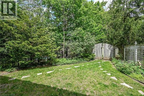 Manicured lawn with stepping stones leading to a wooden gate, framed by mature trees and lush landscaping - 2 Summit Circle, Simcoe, ON - Outdoor
