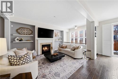 Living area featuring a fireplace with a stone surround and white mantel, built-in shelving, wood-finish flooring, and a glass-paned door with white shutters - 2466 Village Common, Oakville, ON - Indoor Photo Showing Living Room With Fireplace