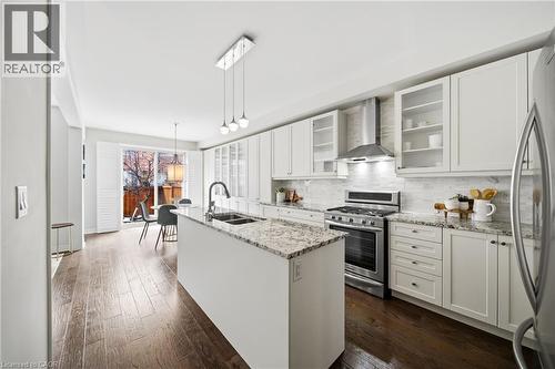 Kitchen featuring a center island with a granite countertop, white cabinetry with glass-front accents, stainless steel appliances, and wood-finish flooring - 2466 Village Common, Oakville, ON - Indoor Photo Showing Kitchen With Double Sink With Upgraded Kitchen