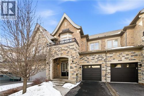 Stone and brick facade residence featuring an arched entryway, double-door main entrance, two garage doors, an upper-level balcony with a metal railing, and a gabled roofline - 2466 Village Common, Oakville, ON - Outdoor With Facade