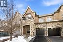 Stone and brick facade residence featuring an arched entryway, double-door main entrance, two garage doors, an upper-level balcony with a metal railing, and a gabled roofline - 2466 Village Common, Oakville, ON  - Outdoor With Facade 