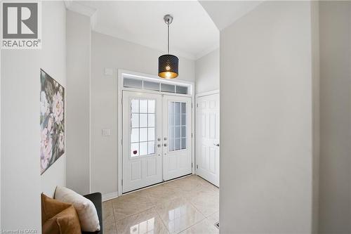 Foyer featuring white double entry doors with decorative glass panels and transom window, light-toned tile flooring, a contemporary pendant light fixture, and crown molding accents - 2466 Village Common, Oakville, ON - Indoor Photo Showing Other Room