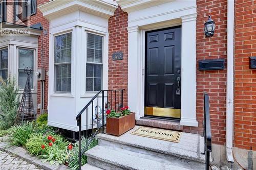 Brick facade featuring a panel door with brass kick plate, white trim, and a black exterior light fixture - 463 Blathwayte Lane, Burlington, ON - Outdoor