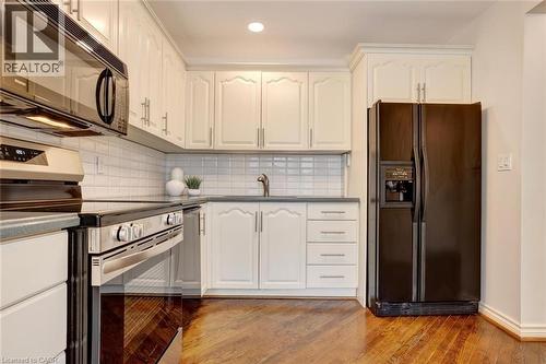 Kitchen featuring white cabinetry with silver-tone hardware, a white subway tile backsplash, a dark countertop, stainless steel appliances, and wood-finish flooring - 463 Blathwayte Lane, Burlington, ON - Indoor Photo Showing Kitchen With Upgraded Kitchen