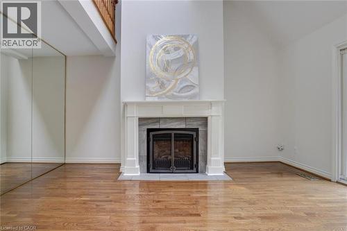 Living area featuring a fireplace with a white mantel and gray tile surround, wood-finish flooring, a mirrored wall, and a white baseboard trim - 463 Blathwayte Lane, Burlington, ON - Indoor Photo Showing Other Room With Fireplace