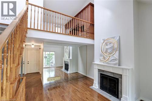Two-story entry featuring wood-finish flooring, a wood staircase with balusters, a fireplace with a white mantel and stone surround, and mirrored wall panels - 463 Blathwayte Lane, Burlington, ON - Indoor With Fireplace