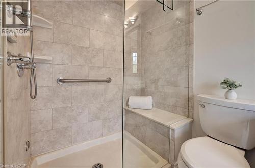 Walk-in shower featuring light-toned rectangular wall tiles, a built-in bench, a chrome-finish handheld shower fixture, a grab bar, and a clear glass enclosure - 463 Blathwayte Lane, Burlington, ON - Indoor Photo Showing Bathroom
