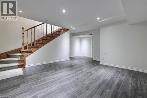 Spacious lower-level area featuring wood-finish flooring, recessed lighting, white walls, and a wooden staircase with carpeted treads - 463 Blathwayte Lane, Burlington, ON - Indoor Photo Showing Other Room
