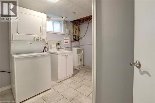 Dedicated laundry area featuring a stacked washer and dryer unit, tiled flooring, a utility sink with white cabinetry, and a frosted window - 463 Blathwayte Lane, Burlington, ON - Indoor Photo Showing Laundry Room