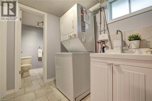 Dedicated laundry area featuring a stacked washer and dryer, a utility sink with a high-arc faucet, and white paneled cabinetry - 463 Blathwayte Lane, Burlington, ON - Indoor Photo Showing Laundry Room