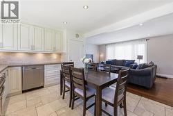 Open-concept kitchen and living area featuring white cabinetry, a tiled backsplash, stainless steel appliances, and a dining space with wood-finish flooring in the adjacent living room - 