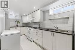 Contemporary kitchen featuring white cabinetry with brushed nickel hardware, dark countertops, white subway tile backsplash, and a double basin stainless steel sink - 