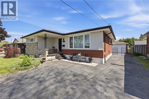 Bungalow exterior featuring a combination of brick and stone cladding, a covered front porch, and a paved driveway leading to a detached garage - 168 Nugent Drive, Hamilton, ON - Outdoor
