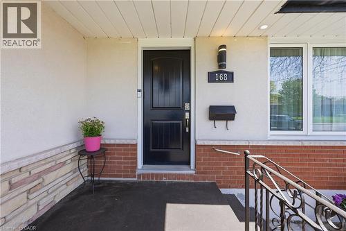 Inviting entryway with a dark paneled door, wrought iron railing, brick facade, stone accent wall, and exterior lighting fixture - 168 Nugent Drive, Hamilton, ON - Outdoor With Exterior