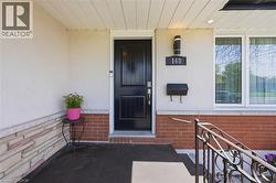 Inviting entryway with a dark paneled door, wrought iron railing, brick facade, stone accent wall, and exterior lighting fixture - 
