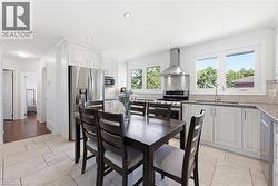 Bright kitchen featuring white cabinetry, stainless steel appliances, light-toned tile flooring, and multiple windows - 