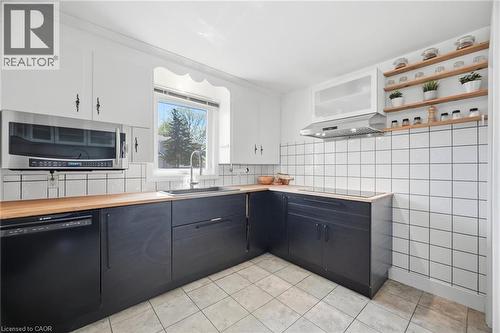 Kitchen featuring dark cabinetry with wood-finish countertops, white subway tile backsplash, and stainless steel appliances including a built-in microwave, dishwasher, and range hood - 94 Clarendon Avenue, Hamilton, ON - Indoor Photo Showing Kitchen