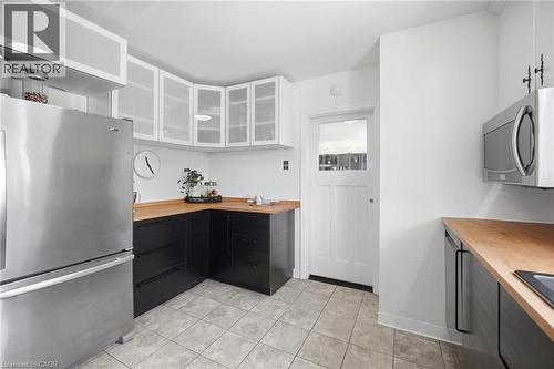 Kitchen featuring stainless steel appliances, black base cabinetry, wood-finish countertops, white upper cabinets with frosted glass panels, and tile flooring - 94 Clarendon Avenue, Hamilton, ON - Indoor Photo Showing Kitchen