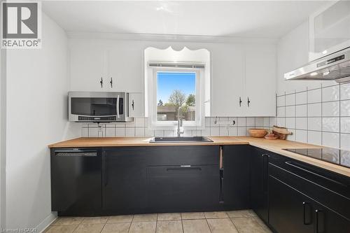 Kitchen featuring black base cabinetry, white upper cabinetry, natural wood-finish countertops, and a white square tile backsplash - 94 Clarendon Avenue, Hamilton, ON - Indoor Photo Showing Kitchen