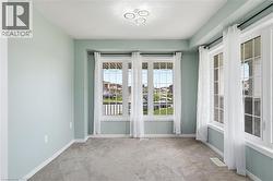 Spacious room featuring multiple large windows with white trim, light green walls, a contemporary ceiling fixture, and neutral carpet flooring - 
